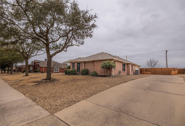 single story home with central air condition unit, fence, concrete driveway, and brick siding