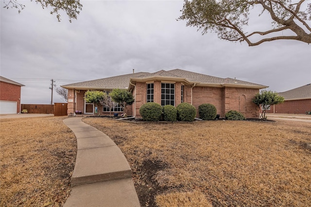 ranch-style home featuring brick siding, fence, a front lawn, and roof with shingles