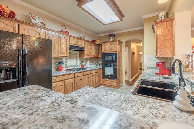 kitchen featuring arched walkways, under cabinet range hood, a sink, black appliances, and crown molding