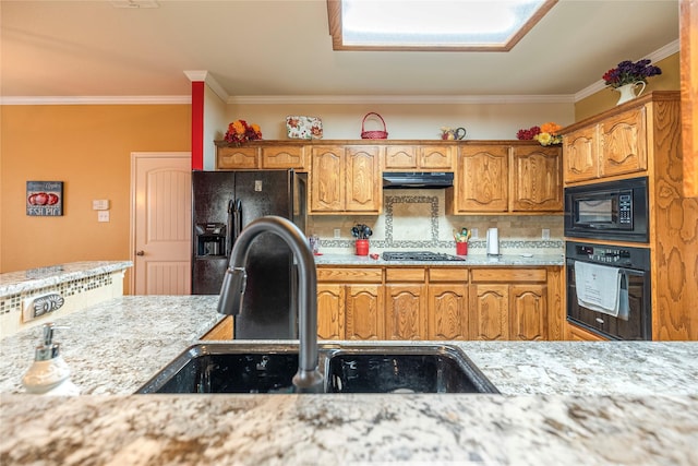 kitchen with under cabinet range hood, a sink, backsplash, black appliances, and brown cabinetry