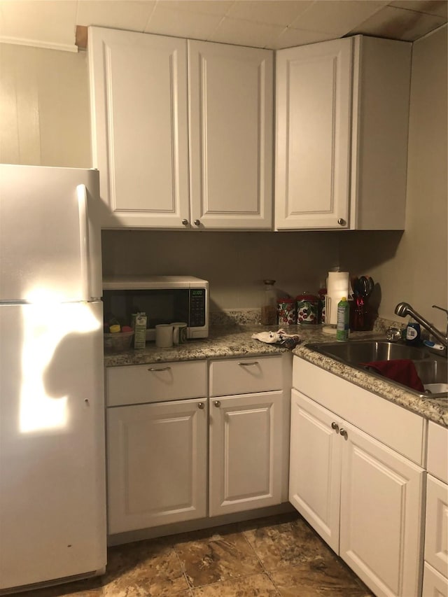 kitchen featuring freestanding refrigerator, white cabinets, a sink, and stainless steel microwave