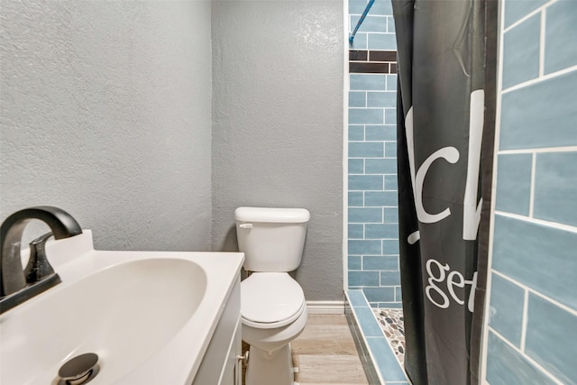 full bath with baseboards, a textured wall, toilet, wood finished floors, and a shower stall