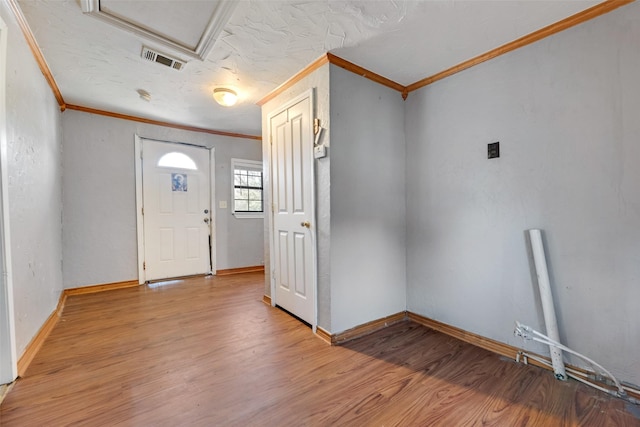 foyer entrance with light wood finished floors, baseboards, visible vents, a textured ceiling, and crown molding