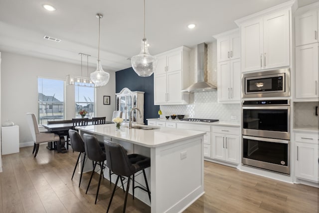 kitchen featuring decorative backsplash, stainless steel appliances, light countertops, wall chimney range hood, and a sink