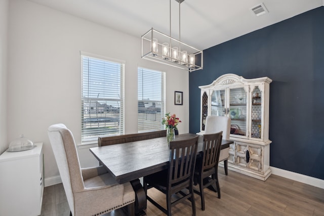 dining area featuring baseboards, a notable chandelier, visible vents, and wood finished floors