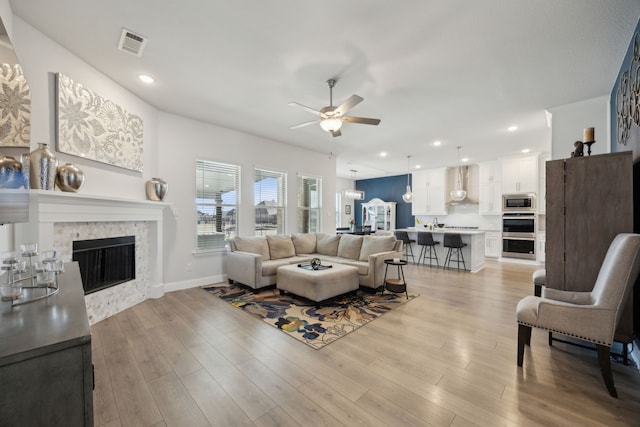 living room with a fireplace, light wood finished floors, recessed lighting, visible vents, and ceiling fan