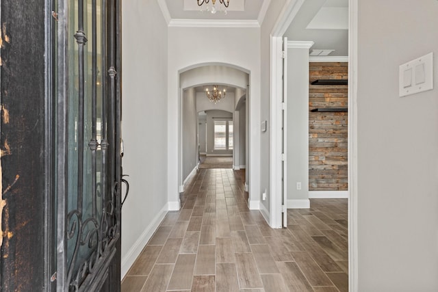 foyer with arched walkways, wood finish floors, an inviting chandelier, ornamental molding, and baseboards