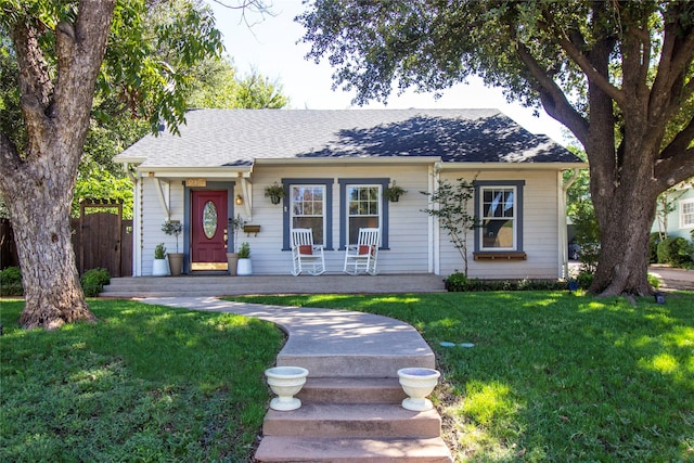 bungalow-style house featuring covered porch, a front lawn, a shingled roof, and fence