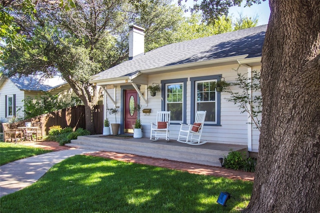 bungalow-style home with a porch, a chimney, a front yard, and a shingled roof