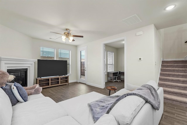 living room featuring stairs, baseboards, wood finished floors, and a glass covered fireplace