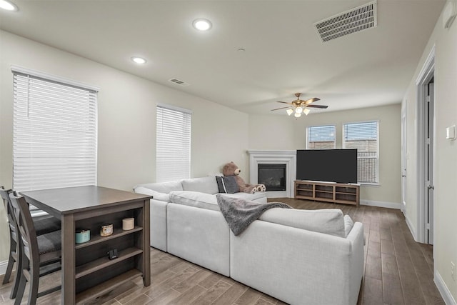 living room featuring a glass covered fireplace, visible vents, recessed lighting, and wood finished floors