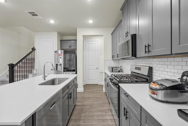 kitchen with stainless steel appliances, a sink, visible vents, light wood-style floors, and light countertops