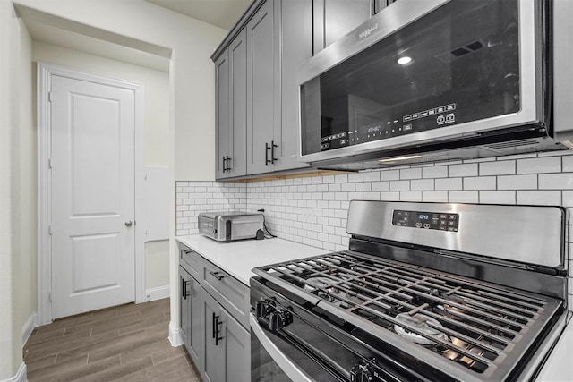 kitchen featuring appliances with stainless steel finishes, wood finish floors, gray cabinets, and decorative backsplash