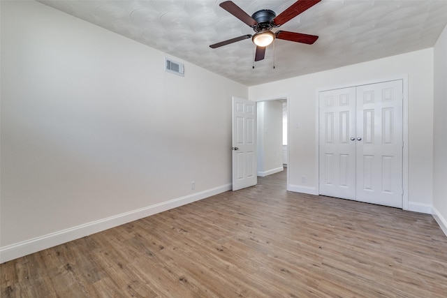 unfurnished bedroom with ceiling fan, light wood-style flooring, visible vents, baseboards, and a closet