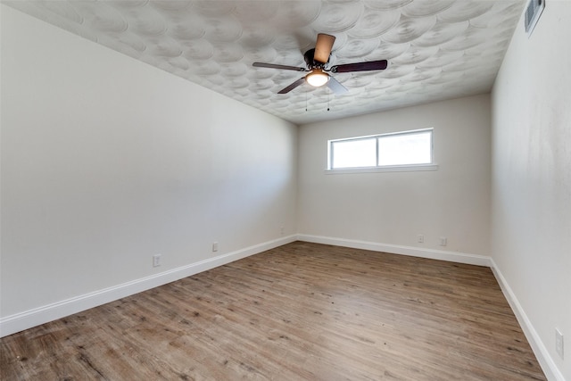 spare room with visible vents, wood finished floors, a ceiling fan, and baseboards