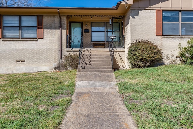 property entrance featuring crawl space, brick siding, a lawn, and covered porch