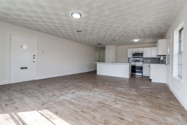 kitchen with stainless steel appliances, wood finished floors, white cabinetry, open floor plan, and a center island