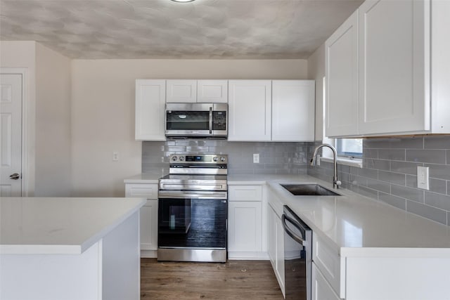 kitchen with white cabinets, wood finished floors, stainless steel appliances, light countertops, and a sink