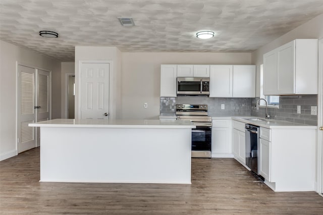 kitchen featuring visible vents, a kitchen island, appliances with stainless steel finishes, wood finished floors, and a sink