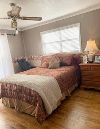 bedroom with wood finished floors, a ceiling fan, and crown molding