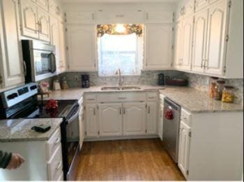 kitchen with white cabinets, light wood-style flooring, a sink, stainless steel appliances, and backsplash