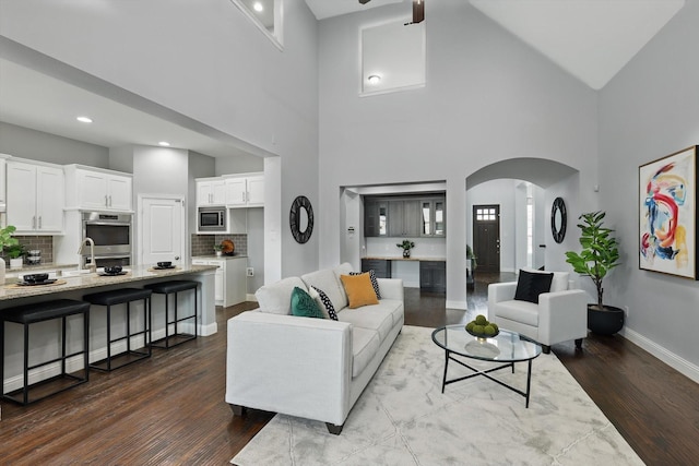 living area featuring baseboards, ceiling fan, dark wood finished floors, a high ceiling, and arched walkways