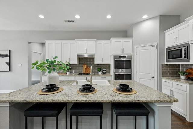 kitchen with visible vents, under cabinet range hood, white cabinets, stainless steel appliances, and a kitchen island with sink