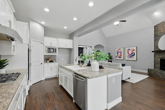 kitchen with open floor plan, a stone fireplace, appliances with stainless steel finishes, dark wood-style floors, and a sink