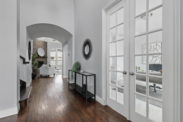 doorway to outside with dark wood finished floors, arched walkways, a fireplace, and baseboards