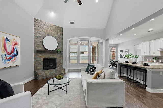 living room featuring baseboards, high vaulted ceiling, a fireplace, ceiling fan, and dark wood-type flooring