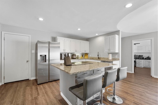 kitchen with white cabinetry, a breakfast bar area, stainless steel refrigerator with ice dispenser, and light wood-type flooring