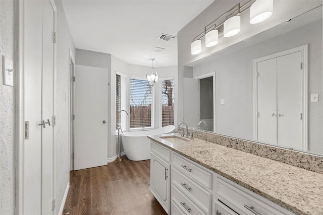 bathroom featuring visible vents, wood finished floors, baseboards, a freestanding bath, and vanity