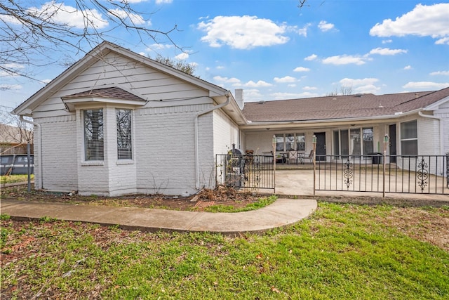 rear view of property with fence, brick siding, a lawn, and a patio area