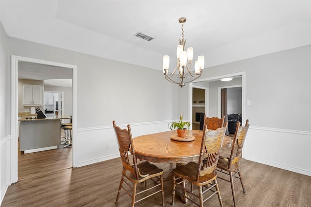 dining room with a notable chandelier, visible vents, a brick fireplace, and wood finished floors