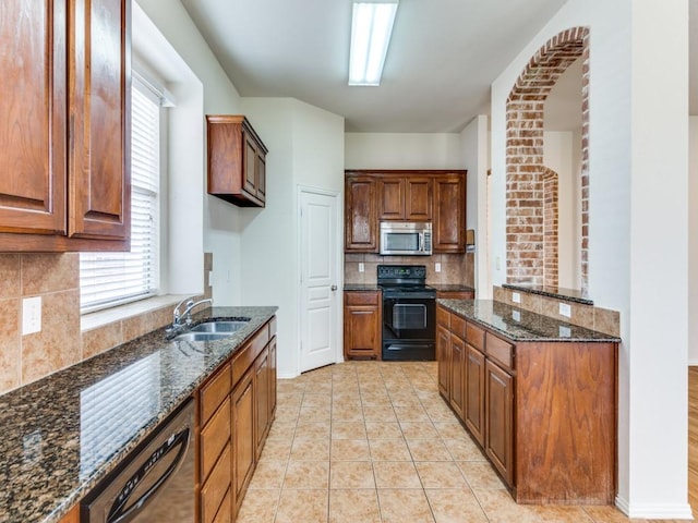 kitchen featuring dark stone countertops, light tile patterned flooring, a sink, and black appliances