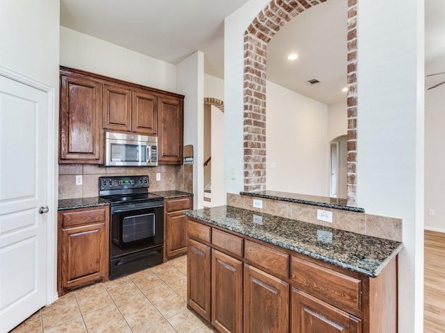 kitchen featuring dark stone counters, black range with electric stovetop, stainless steel microwave, and tasteful backsplash