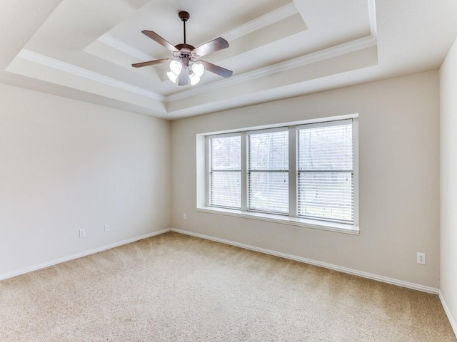 spare room with carpet floors, a tray ceiling, ornamental molding, a ceiling fan, and baseboards