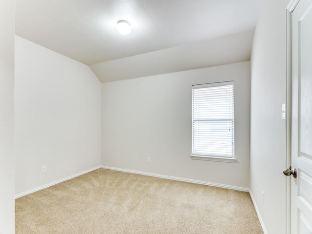 spare room with light colored carpet, vaulted ceiling, and baseboards