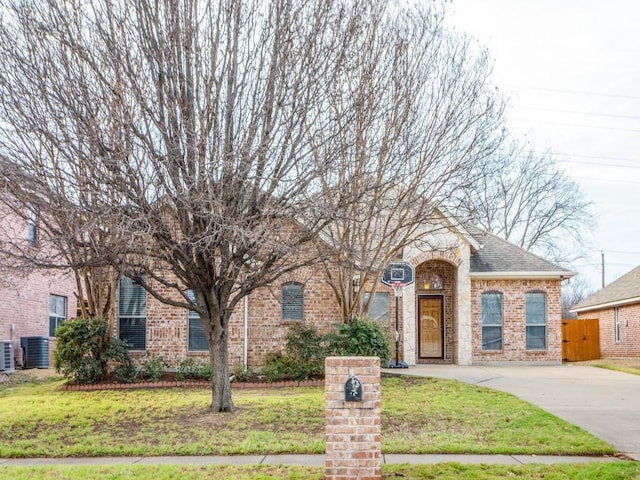 obstructed view of property with brick siding, a shingled roof, fence, central AC, and a front yard