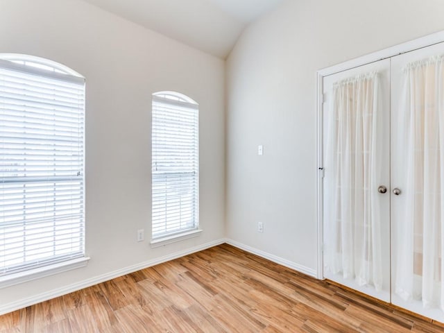 spare room with lofted ceiling, light wood-type flooring, and baseboards