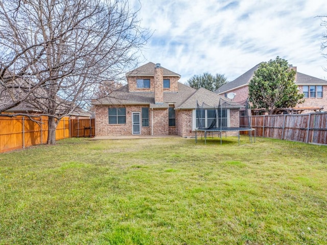 rear view of property with a trampoline, a fenced backyard, a yard, and brick siding