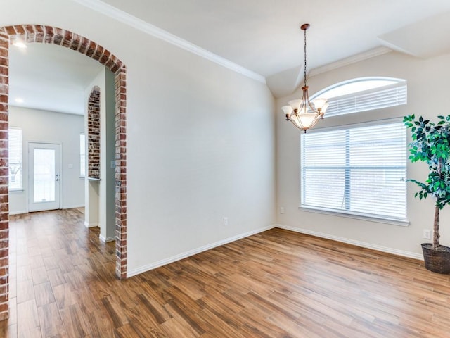 unfurnished room featuring arched walkways, wood finished floors, an inviting chandelier, crown molding, and a healthy amount of sunlight