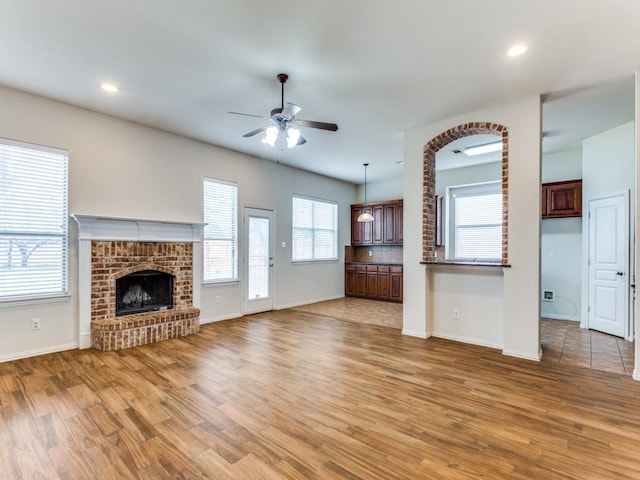 unfurnished living room featuring a brick fireplace, ceiling fan, light wood-style flooring, and baseboards