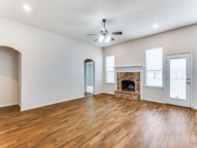 unfurnished living room featuring arched walkways, a fireplace, a ceiling fan, wood finished floors, and baseboards