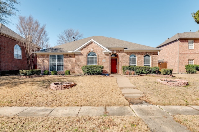 single story home with a shingled roof, brick siding, and a fire pit