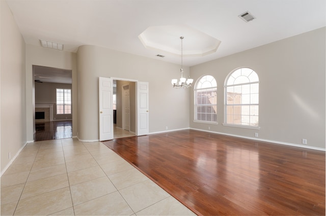 spare room with a tray ceiling, a fireplace, visible vents, an inviting chandelier, and wood finished floors