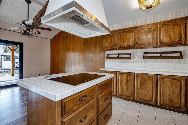 kitchen featuring tile countertops, brown cabinetry, extractor fan, and backsplash