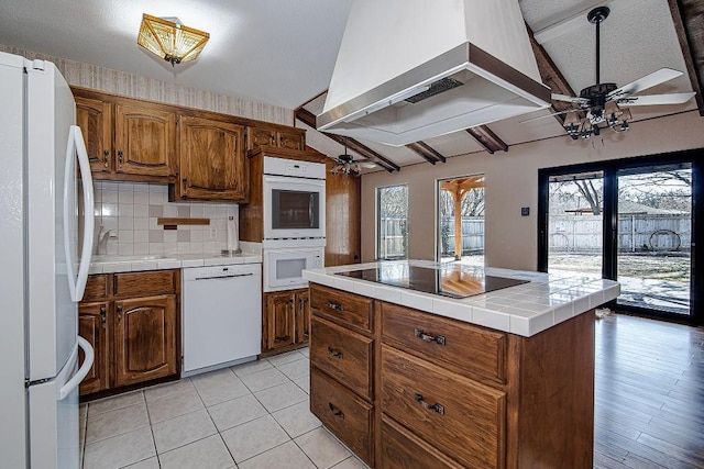 kitchen with white appliances, wall chimney exhaust hood, tile counters, and ceiling fan