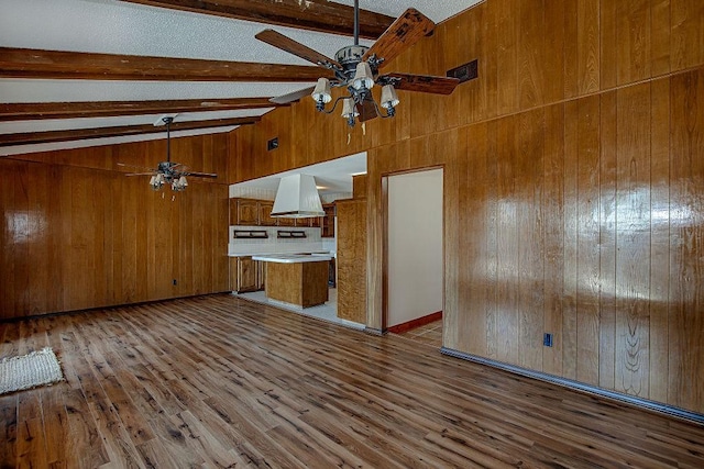 kitchen with brown cabinetry, beam ceiling, wooden walls, and wood finished floors