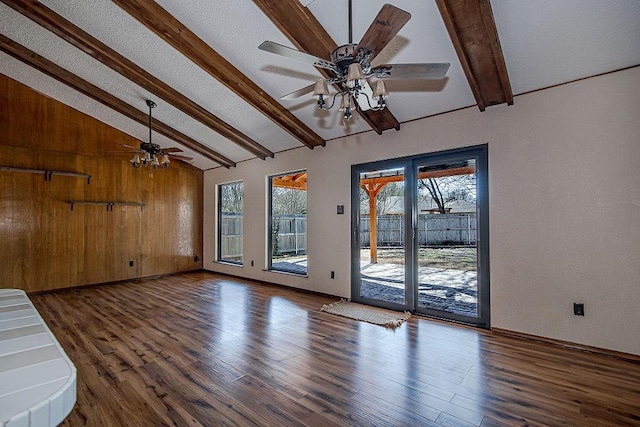 unfurnished living room featuring ceiling fan, wood finished floors, vaulted ceiling with beams, a textured ceiling, and wood walls